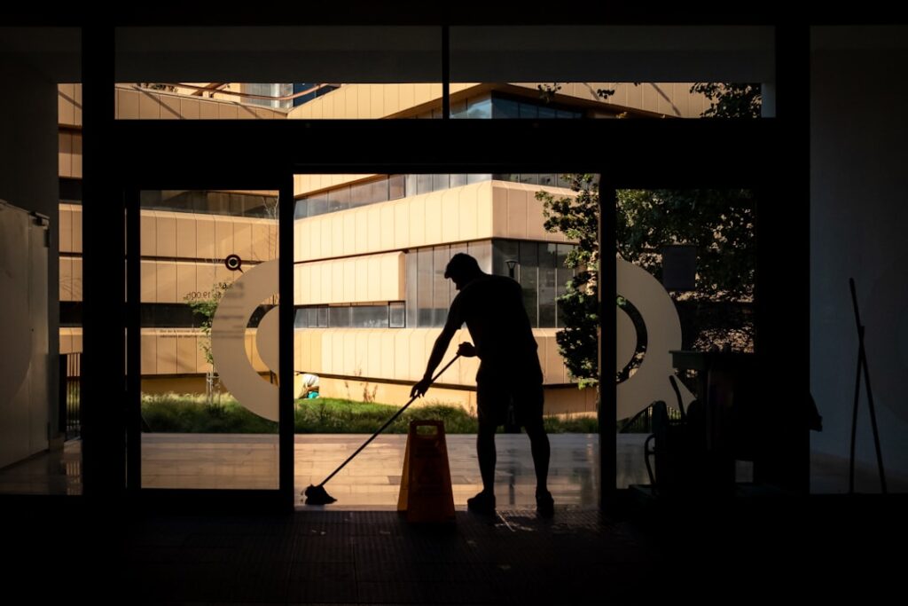Reinigungskraft in Silhouette vor großer Fensterfront